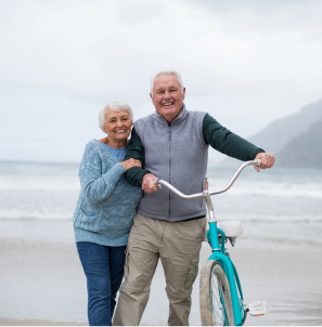 senior-couple-standing-with-bicycle-beach 1